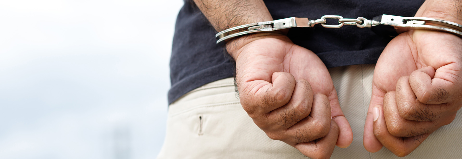 Arrest the offender Prison male criminal standing in handcuffs with hands behind back