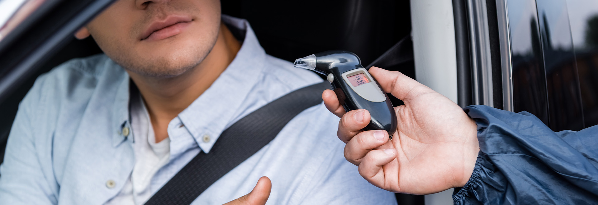cropped view of driver taking breathalyzer from policeman while sitting in car