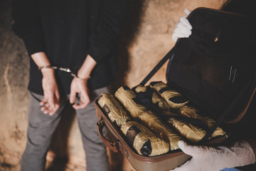 person in handcuffs and briefcase full of drugs